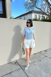 a lady in a blue collarless knit jacket and a pair of white shorts